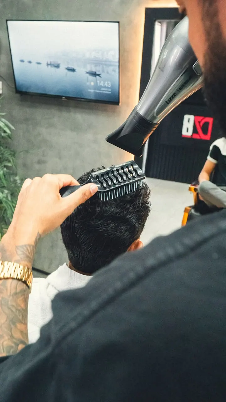Barbeiro finalizando penteado com secador e escova